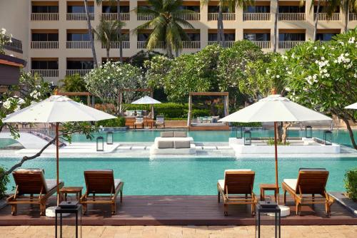 a pool with chairs and umbrellas next to a building at Dusit Thani Hua Hin in Cha Am