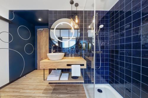 bagno piastrellato blu con lavandino e specchio di H2 Hotel Düsseldorf City a Dusseldorf