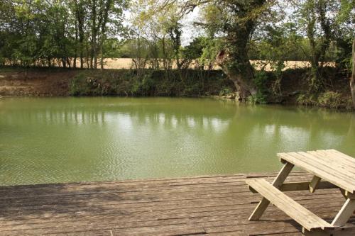 a wooden picnic table sitting on a dock next to a river at The Kestrel Shepherd Hut, Whitehouse Farm in Stowmarket