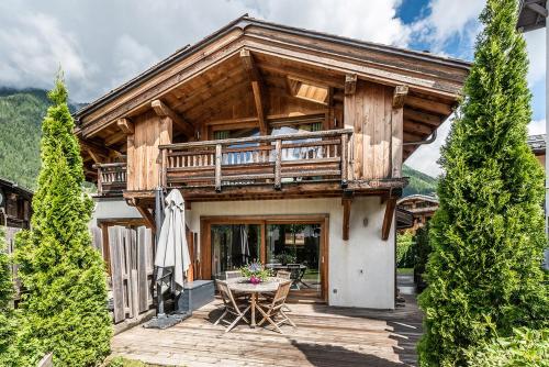 a wooden house with a balcony and a table at Eden Hotel, Apartments and Chalet Chamonix Les Praz in Chamonix-Mont-Blanc