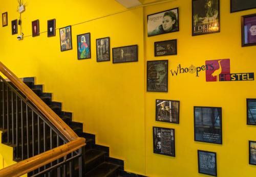 a yellow wall with pictures on it with stairs at Whoopers Hostel Kasol in Kasol