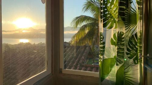 a window with a view of the ocean and a palm tree at Varanda Suspensa em São Sebastião. in São Sebastião