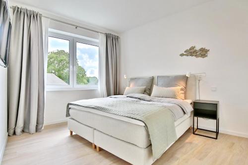 a white bedroom with a bed and a window at Strandperle Ostsee Suite 3 in Niendorf