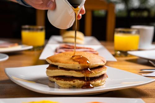 a person pouring syrup onto a stack of pancakes on a plate at Estancia San Antonio in Guasca