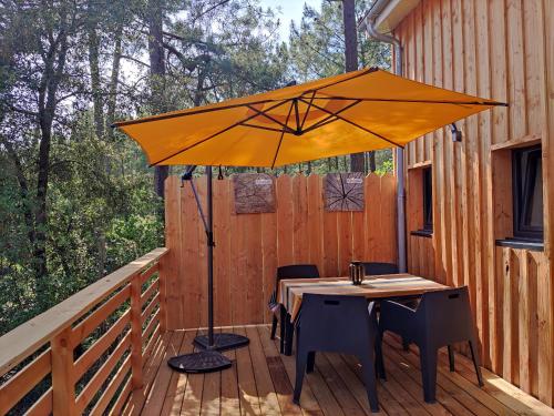 an orange umbrella on a deck with a table and chairs at Lodge 2 étoiles la tête dans les pins les pieds dans l eau in Lacanau
