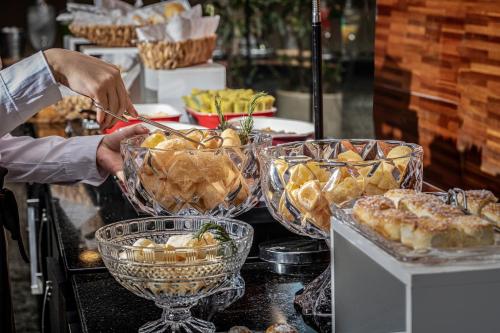 a person preparing food in glass bowls on a buffet at SJ Premium Hotels By Atlantica in Goiânia