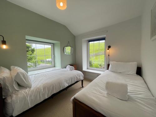 dwa łóżka w pokoju z dwoma oknami w obiekcie Cosy country cottage with log fireplace and views w mieście Kendal