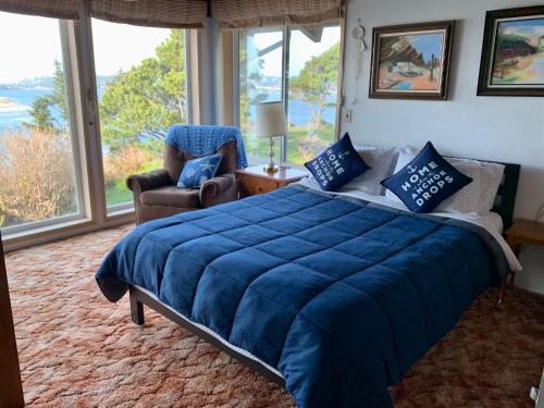 a bedroom with a blue bed and a chair and windows at Panoramic Promontory: Bay View Beach House in Waldport