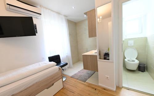 a bathroom with a toilet and a tv on a wall at Enjoyit Rooms in Velden am Wörthersee