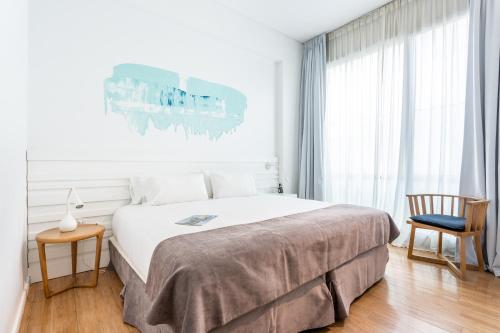 a white bedroom with a large bed and a chair at Hotel BA Jardines Palermo in Buenos Aires