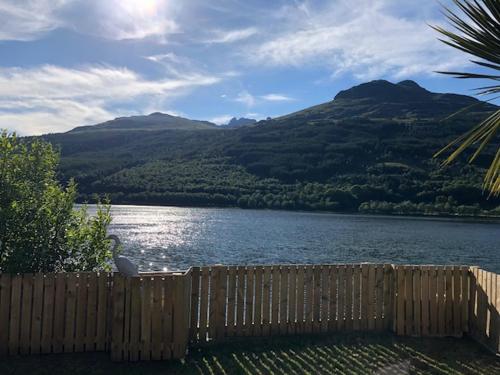 a wooden fence next to a lake with mountains at Heron’s View in Arrochar