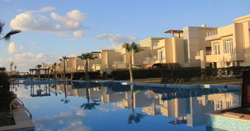 a swimming pool with palm trees and buildings in the background at North coast sedra resort villa قريه سيدرا الساحل الشمالي in Alexandria