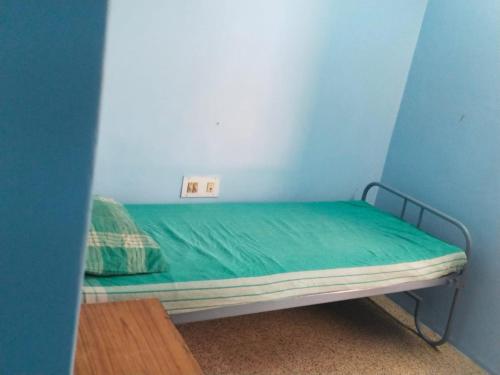 a small bed in a blue room with a green sheet at Zama Lodge in Chennai