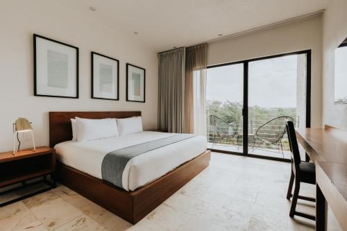 a bedroom with a bed and a desk and windows at The Strabon Tulum in Tulum