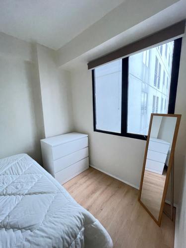 Schlafzimmer mit einem Bett, einem Spiegel und einem Fenster in der Unterkunft Moagi Stay Alamanda - Netflix Ready! at Bassura City Apartment in Jakarta