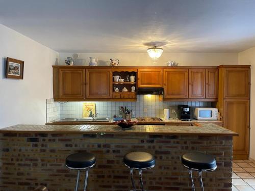 una cocina con armarios de madera y una barra con taburetes en Maison de campagne chaleureuse et au calme, en Léotoing
