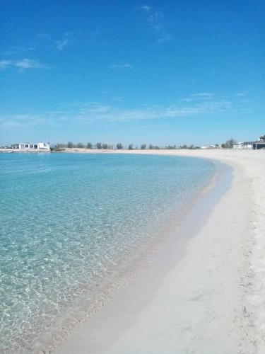 a white beach with blue water and buildings in the background at B&B Vacanze Salento in Torre San Giovanni Ugento