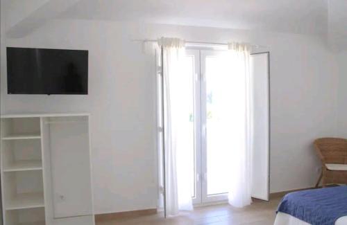 a bedroom with a tv on the wall and two windows at Sudoeste Guest House in Odeceixe