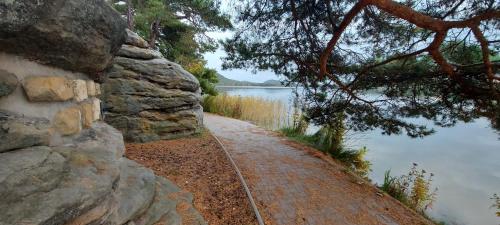 a path next to a rock wall next to a lake at Apartmány Kousek od jezera in Doksy