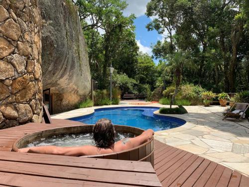 a woman laying in a hot tub next to a pool at Casa da Pedra Atibaia Clube da Montanha in Atibaia