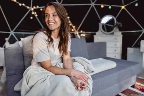 a woman sitting on a couch under a blanket at Glamping Julared in Mullsjö