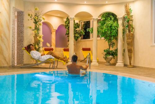 un homme dans une piscine avec une femme assise sur une chaise dans l'établissement La Montanina Hotel in Val di Non, à Malosco