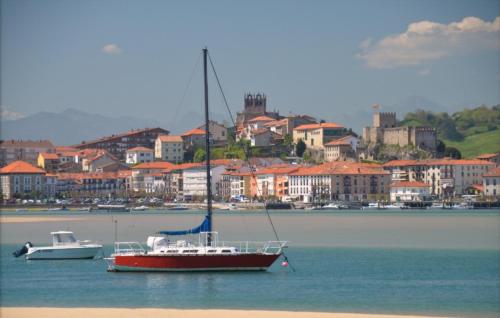 a boat in the water with a city in the background at Apartamentos Costa Norte in San Vicente de la Barquera
