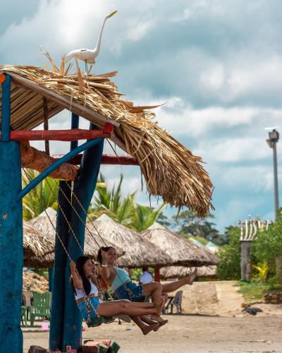 three women sitting under a straw umbrella on the beach at Hotel Agroturistico Palma Vino in Arboletes