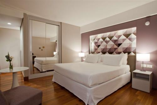a bedroom with a large white bed and a mirror at NH Collection Curitiba in Curitiba
