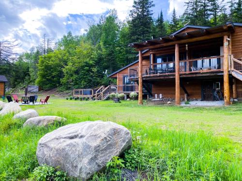 a log cabin with a large rock in front of it at Artemis Log Cabin with Spa & Mountain View in Sainte-Lucie-de-Doncaster