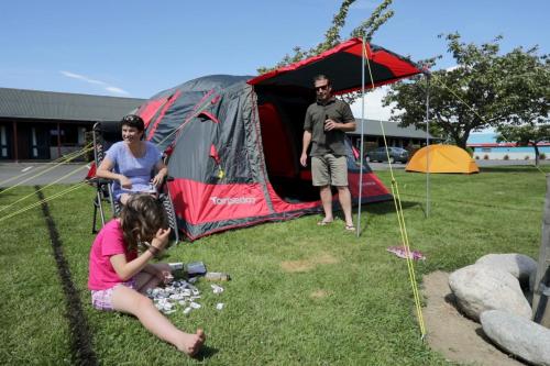 a girl sitting on the grass in front of a tent at Te Anau Top 10 Holiday Park and Motels in Te Anau