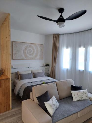 a bedroom with a bed and a couch and a ceiling fan at Arena Negra in Tarajalejo