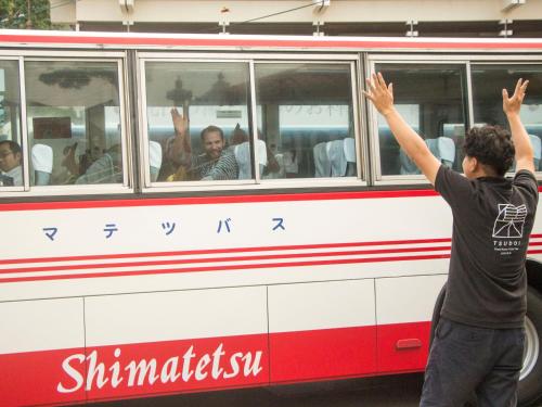 a man standing in front of a red and white bus at TSUDOI guest house in Unzen