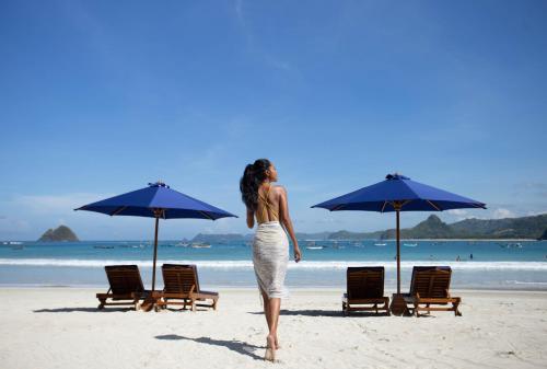 a woman walking on the beach with chairs and umbrellas at Tropik Resort Lombok in Selong Belanak