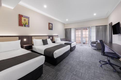 a hotel room with two beds and a desk at Quality Hotel Melbourne Airport in Melbourne