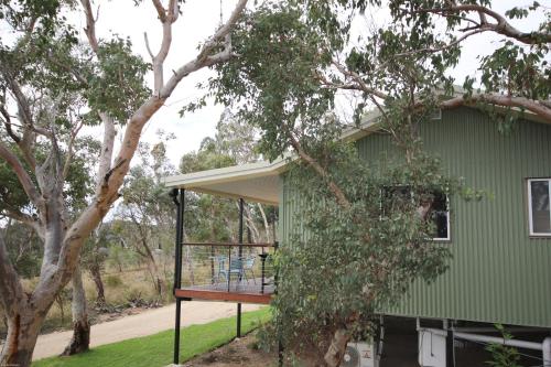 a green house with a porch and a tree at Glen Lough Cabins in Glen Aplin
