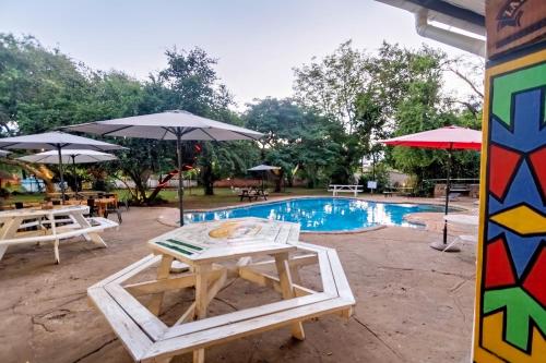 a pool with tables and umbrellas and a table and chairs at Shoestrings Backpackers Lodge Vic Falls in Victoria Falls