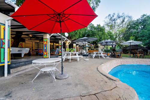 a red umbrella and a table and chairs next to a pool at Shoestrings Backpackers Lodge Vic Falls in Victoria Falls