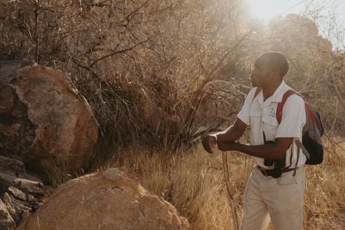 a man with a backpack standing in a field at Ai Aiba - The Rock Painting Lodge in Omaruru