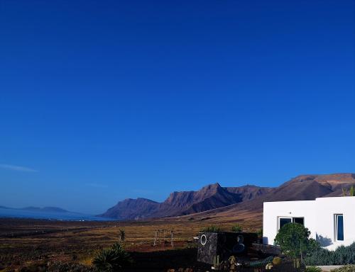 a white building in a field with mountains in the background at EL REFUGIO in Famara