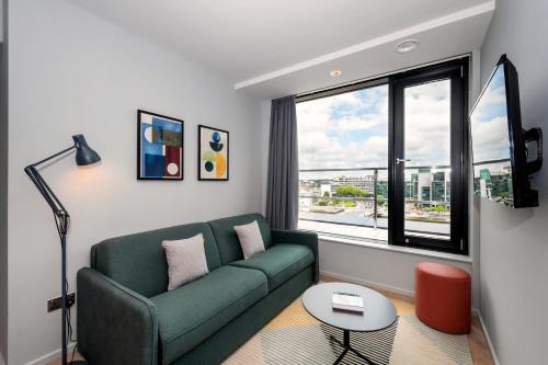 a living room with a green couch and a large window at Staycity Aparthotels Dublin City Quay in Dublin