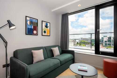 a living room with a green couch and a large window at Staycity Aparthotels Dublin City Quay in Dublin