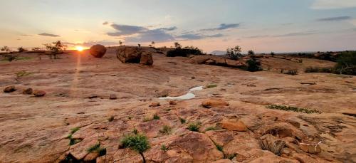 a sunset over a rocky field with the sun setting at Ai Aiba - The Rock Painting Lodge in Omaruru
