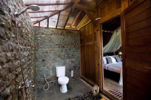a bathroom with a toilet in a room with a bed at Sebatu Tulen Villa in Tegalalang