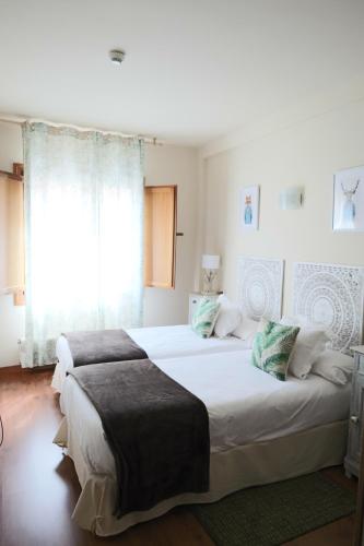 a white bedroom with two beds and a window at Naquela Castroviejo in Castroviejo