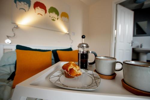 a table with a cupcake on a plate and two cups at Chichele House, sleeps 8, Nr Rushden Lakes, allocated parking, corporate welcome in Higham Ferrers