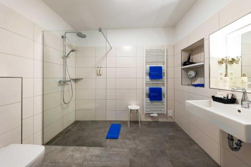 baño blanco con ducha y alfombra azul en Hotel Landhaus Steinfeld, en Greetsiel