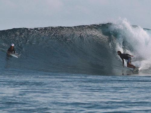 two people riding a wave on surfboards in the ocean at Palm Gate Maldives in Thulusdhoo