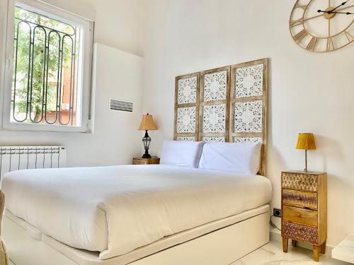 a white bedroom with a large bed and a clock at Charming Madrid Studio - Largas Estancias in Madrid