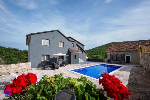 een huis met een zwembad en rode bloemen bij Villa with a heated private pool, parking, BBQ in Petričevići